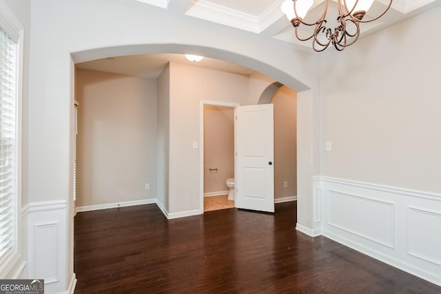 unfurnished room with arched walkways, a decorative wall, dark wood-style flooring, ornamental molding, and wainscoting