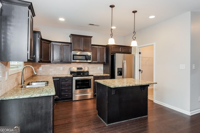 kitchen featuring tasteful backsplash, a kitchen island, decorative light fixtures, stainless steel appliances, and a sink