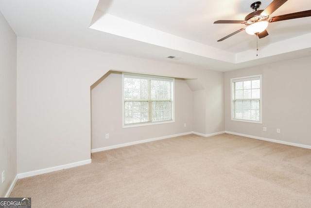 empty room featuring light colored carpet, a raised ceiling, visible vents, and baseboards