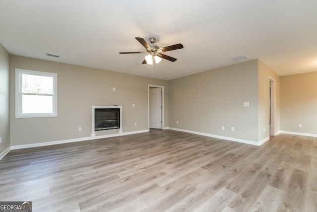 unfurnished living room featuring light wood-type flooring, a glass covered fireplace, visible vents, and baseboards