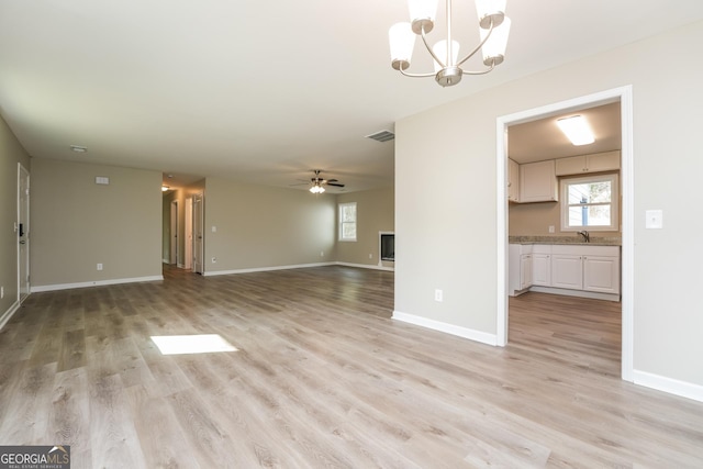 unfurnished living room featuring ceiling fan with notable chandelier, light wood finished floors, and baseboards