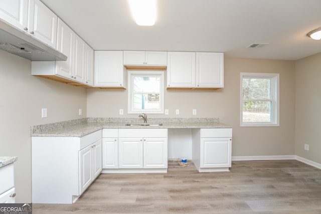 kitchen featuring a healthy amount of sunlight, light wood finished floors, white cabinetry, and a sink