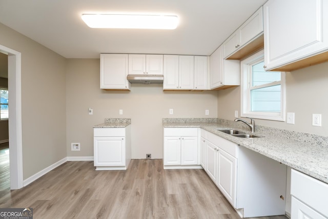 kitchen featuring light wood-style flooring, light stone counters, under cabinet range hood, white cabinetry, and a sink