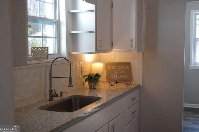 kitchen featuring open shelves, decorative backsplash, white cabinetry, a sink, and light stone countertops