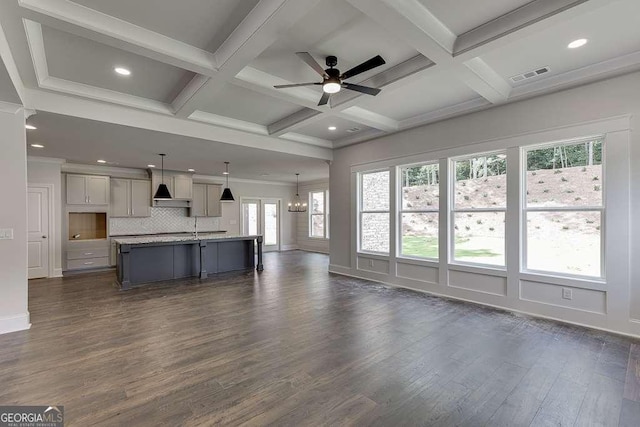 unfurnished living room featuring ceiling fan with notable chandelier, coffered ceiling, visible vents, beam ceiling, and dark wood-style floors