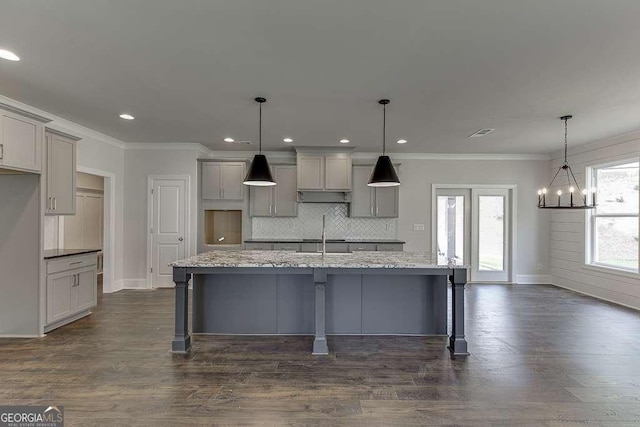 kitchen featuring hanging light fixtures, light stone countertops, a center island with sink, and gray cabinets