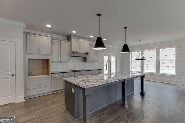 kitchen with a center island with sink, decorative light fixtures, light stone countertops, gray cabinets, and a sink