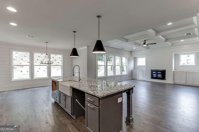 kitchen featuring light stone counters, coffered ceiling, a sink, open floor plan, and a center island with sink