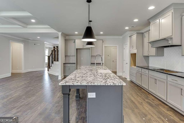 kitchen with black electric cooktop, a kitchen island with sink, gray cabinetry, dark wood-type flooring, and decorative light fixtures