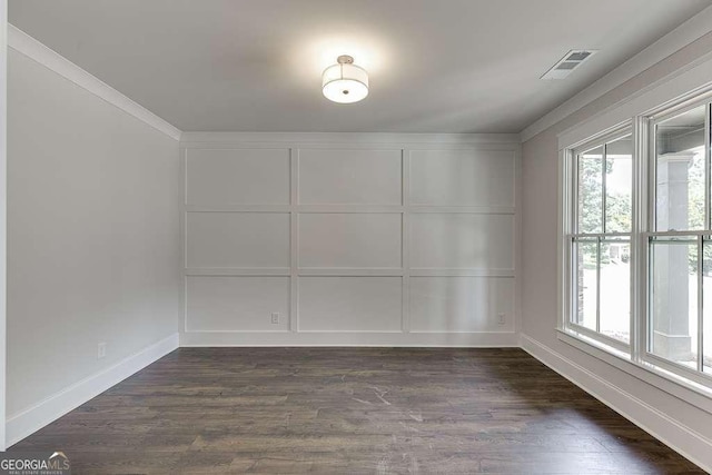 empty room with crown molding, dark wood finished floors, visible vents, and a decorative wall