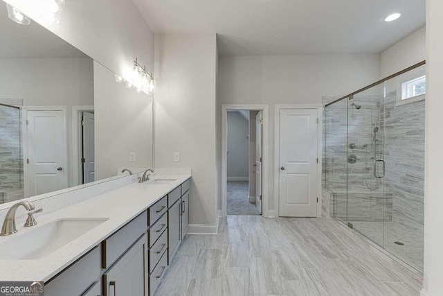 full bathroom featuring double vanity, a stall shower, baseboards, and a sink