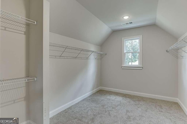 walk in closet featuring visible vents, vaulted ceiling, and light colored carpet