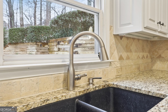 interior details featuring white cabinetry, light stone counters, backsplash, and a sink