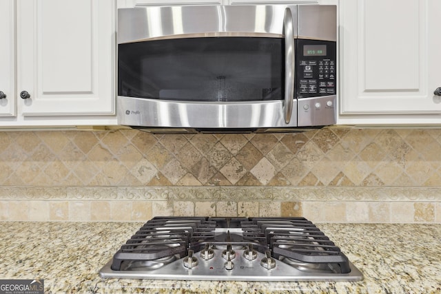 details featuring tasteful backsplash, appliances with stainless steel finishes, white cabinetry, and light stone countertops