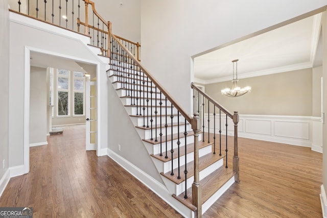 stairway with crown molding, baseboards, a chandelier, wood finished floors, and a decorative wall