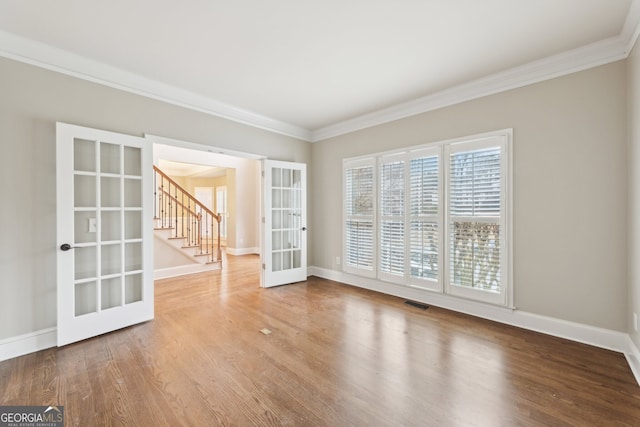 empty room featuring french doors, wood finished floors, ornamental molding, and stairway