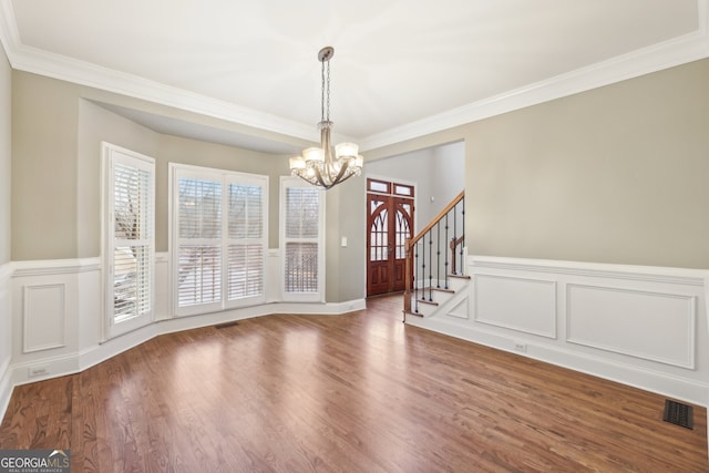 unfurnished dining area with visible vents, wood finished floors, an inviting chandelier, crown molding, and stairs