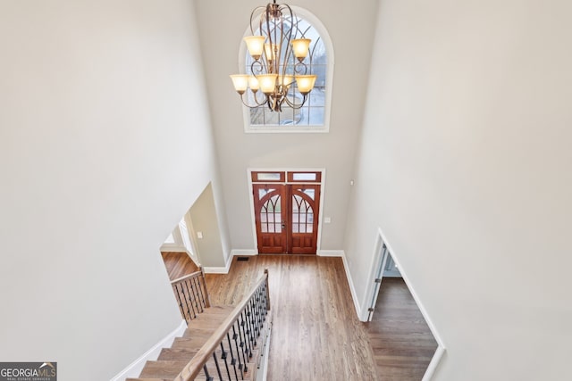 foyer entrance with wood finished floors, baseboards, stairs, a towering ceiling, and a chandelier