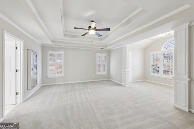 empty room featuring a tray ceiling, decorative columns, light colored carpet, and a wealth of natural light