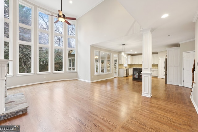 unfurnished living room with baseboards, decorative columns, ceiling fan, crown molding, and light wood-type flooring