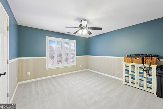 carpeted spare room with visible vents, wainscoting, and ceiling fan