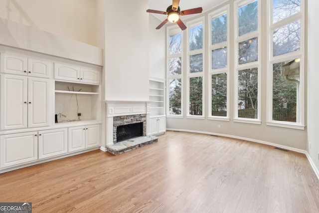 unfurnished living room featuring visible vents, baseboards, a high ceiling, light wood-style flooring, and a stone fireplace