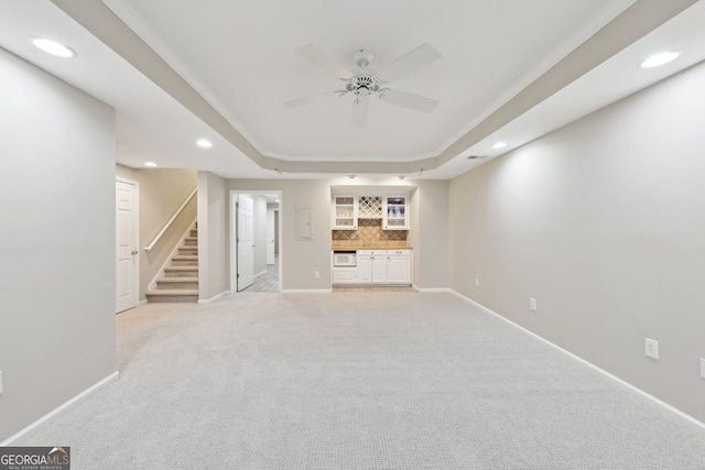 unfurnished living room with recessed lighting, a tray ceiling, a bar, and stairway