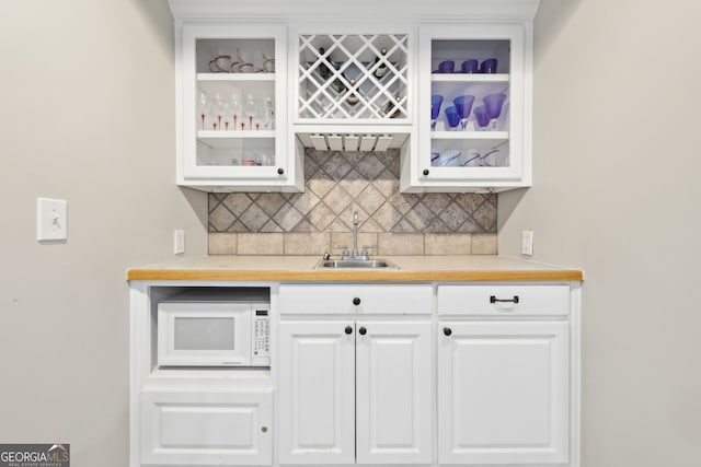 bar featuring white microwave, decorative backsplash, wet bar, and a sink