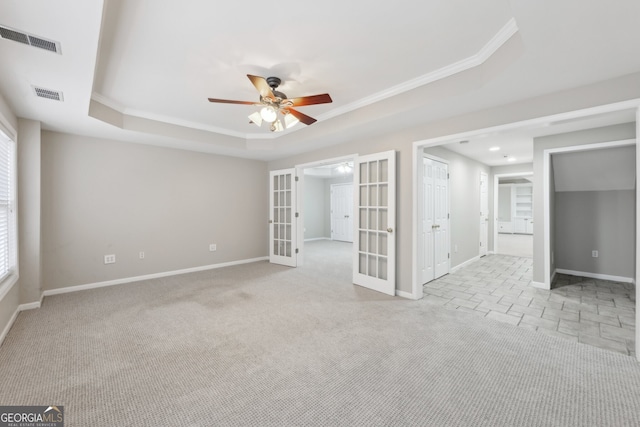 empty room featuring a raised ceiling, french doors, visible vents, and light carpet