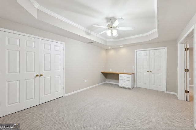 unfurnished bedroom with built in desk, light colored carpet, a raised ceiling, and ornamental molding