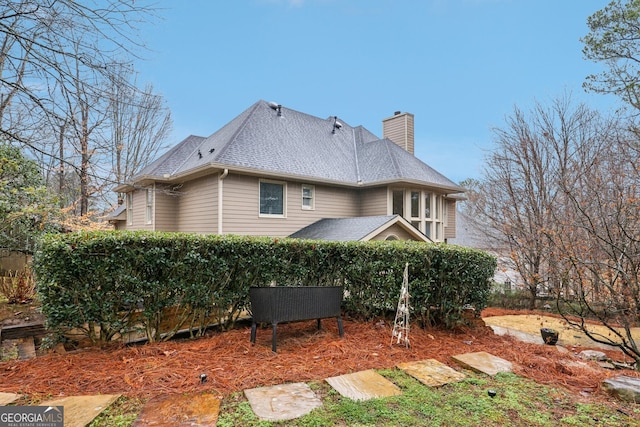 rear view of property featuring a shingled roof and a chimney