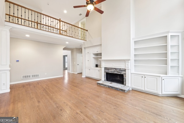 unfurnished living room featuring visible vents, light wood-style flooring, a ceiling fan, a high ceiling, and a fireplace