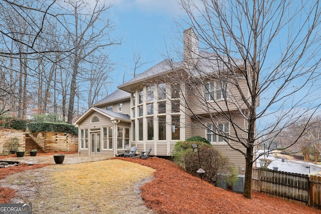 rear view of house featuring central AC unit, fence, a sunroom, and a chimney