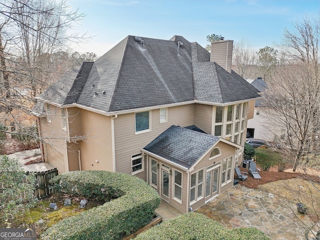 rear view of house featuring fence, a sunroom, a shingled roof, a chimney, and a patio area