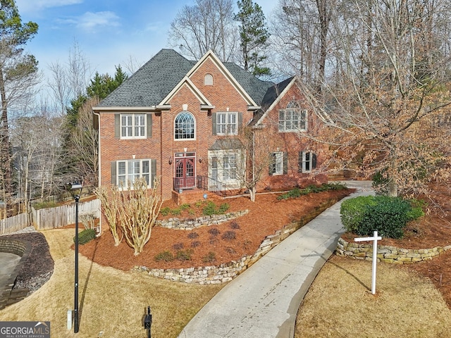 view of front of property featuring fence, brick siding, and roof with shingles