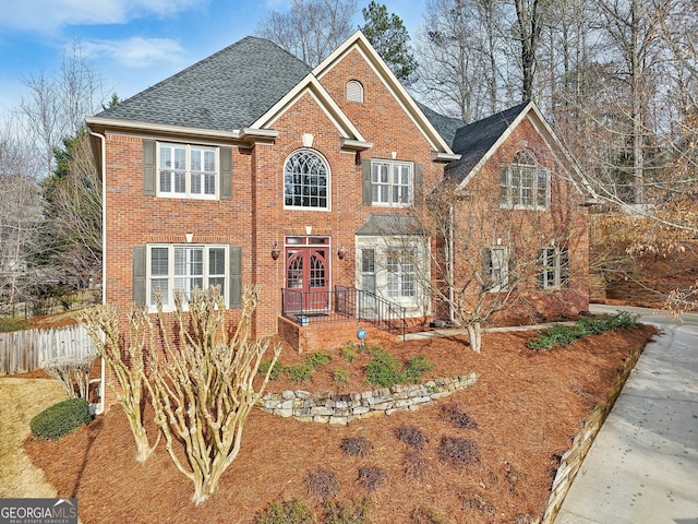 view of front facade with fence, brick siding, and a shingled roof