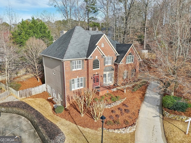 view of front of home featuring brick siding, a shingled roof, a chimney, and fence