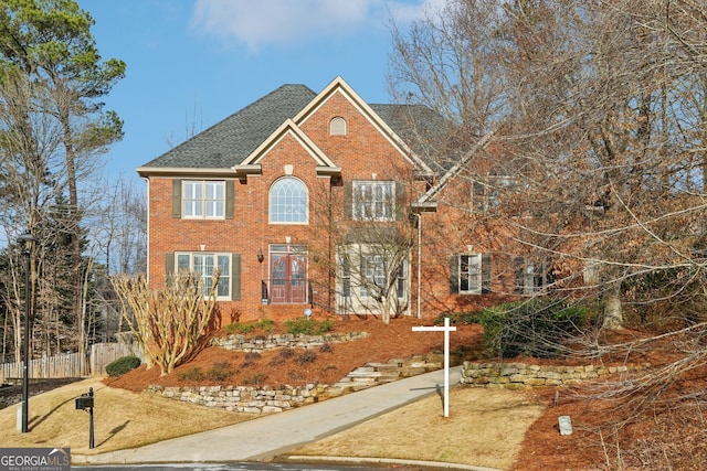 colonial-style house featuring brick siding, a shingled roof, and fence