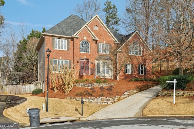 view of front of house with fence, brick siding, and a shingled roof