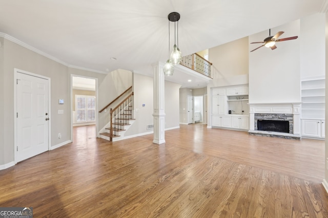 unfurnished living room with crown molding, stairs, a fireplace, light wood-style floors, and ornate columns