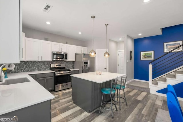 kitchen featuring pendant lighting, stainless steel appliances, white cabinetry, a sink, and a kitchen island