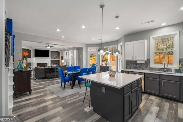 kitchen with a center island, light countertops, hanging light fixtures, white cabinetry, and a sink