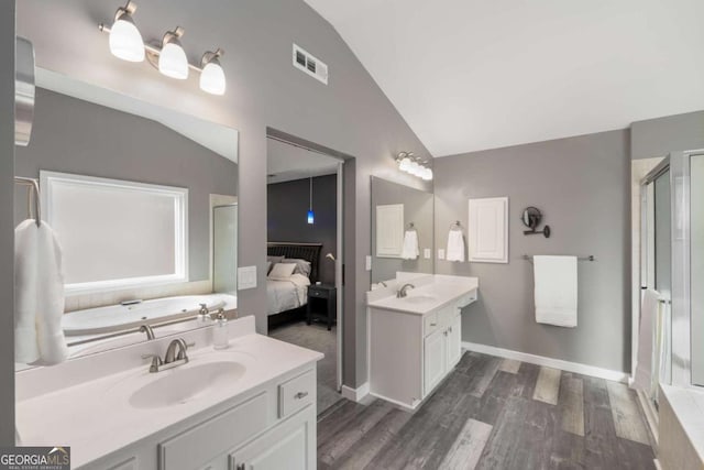 ensuite bathroom featuring visible vents, a sink, vaulted ceiling, ensuite bath, and wood finished floors