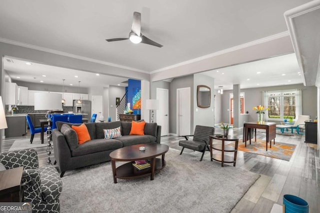 living room featuring ceiling fan, ornamental molding, stairway, and light wood-style floors