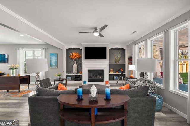 living room featuring visible vents, baseboards, light wood-type flooring, a glass covered fireplace, and crown molding