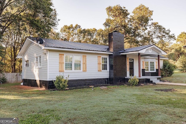 view of front of house featuring a chimney, fence, metal roof, and a front yard