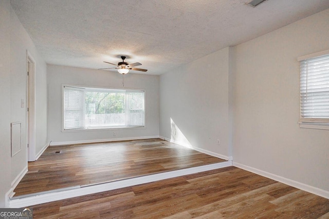 empty room featuring a textured ceiling, wood finished floors, a ceiling fan, and baseboards