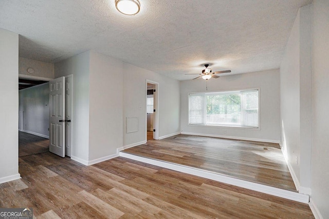 unfurnished room with a ceiling fan, a textured ceiling, baseboards, and wood finished floors