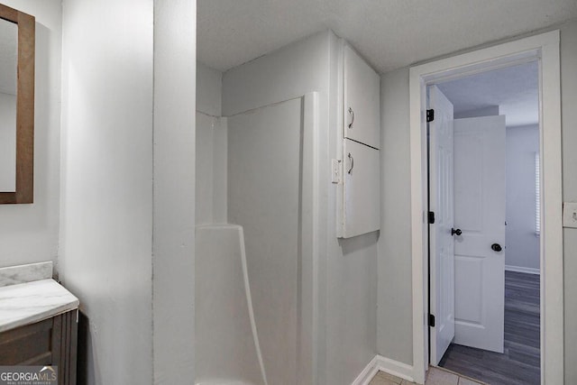 bathroom featuring baseboards, walk in shower, wood finished floors, and vanity