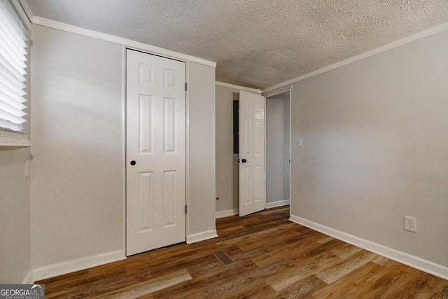 unfurnished bedroom with baseboards, ornamental molding, wood finished floors, a textured ceiling, and a closet